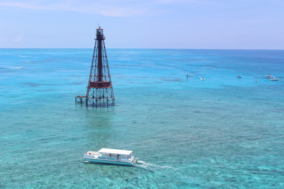 An aerial view of the catamaran cruising past a Keys reef lighthouse over vivid blue reef flats