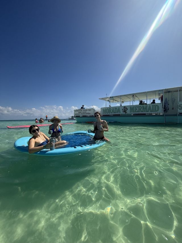 Guests on a paddleboard beside the Morada Mermaid hull in crystal-clear water lit by a sunbeam
