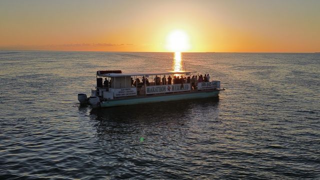 Aerial view of the Marathon Mermaid catamaran full of guests under a glowing low sun with its reflection streaking across the water